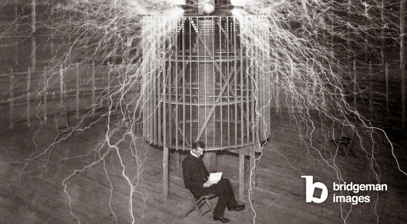 Nikola Tesla assis dans son laboratoire de Colorado Springs avec son "émetteur grossissant"